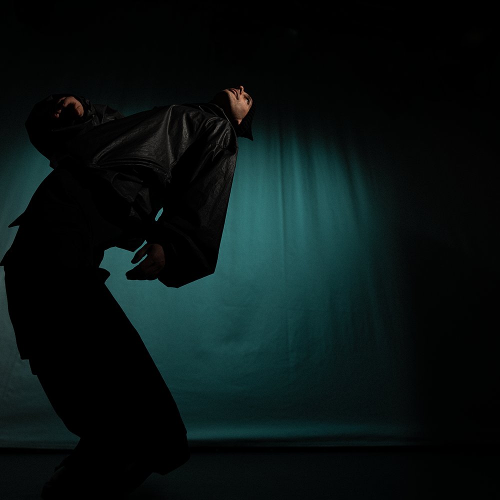 Chronis leaning back in teal stage light